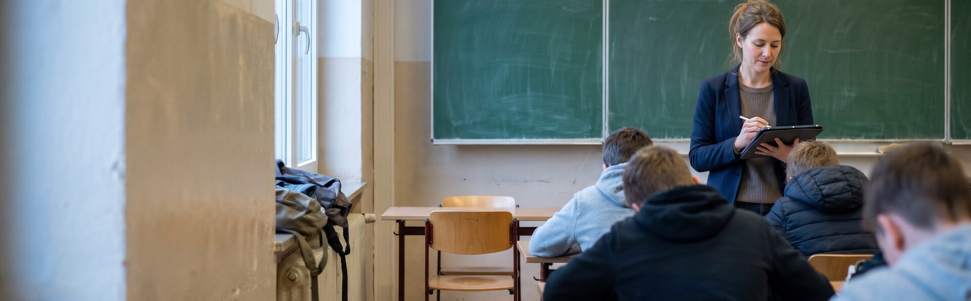 Lehrerin erfasst zu Unterrichtsbeginn die Anwesenheit am Tablet, ein Platz in der Klasse ist leer