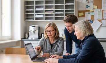 Drei Lehrkräfte vergleichen im Lehrerzimmer am Laptop Schulsoftware